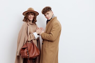 a happy couple in love is standing in beige stylish autumn coats on a white background and a man is holding a woman's hands smiling pleasantly
