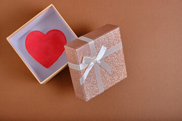 Open gift box with heart inside brown background is tied with beige ribbon with bow.