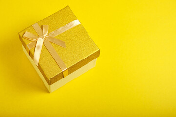 Golden gift box is tied with ribbon with bow yellow background.