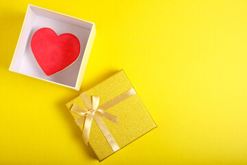 Open gift box in gold color with ribbon and bow with heart inside on yellow background.