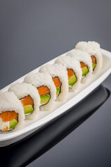 salmon roll with avocado and cheese on black background with reflection
