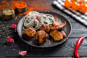 Kebab of pork with red onion on dark stone plate on black wooden table