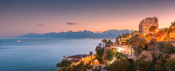 Naklejka premium Aerial panoramic cityscape view of Antalya resort town with hotels and buildings and Taurus mountains in the background during majestic sunset twilight