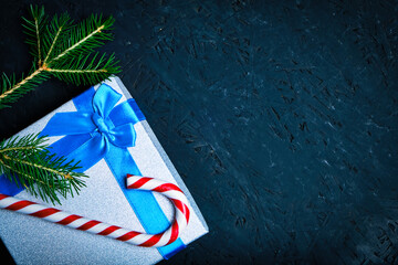 Christmas gift box tied with blue ribbon with bow with green Christmas tree and caramel on dark background.