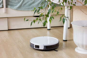 White robotic vacuum cleaner cleaning at home.