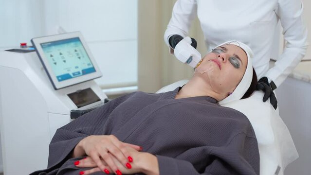 beautician is using apparatus with broadband light for rejuvenation and curing face skin