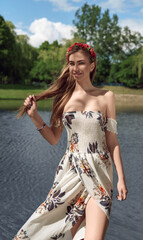 Pretty woman wearing floral dress and flowers wreath while standing in blue lake