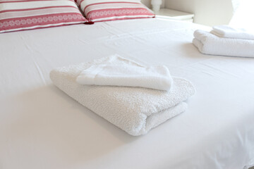 Fototapeta na wymiar White folded towels on a hotel bed with white sheets.