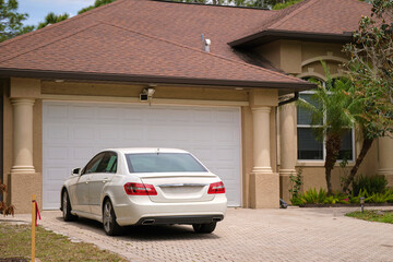 Vehicle parked in front of wide garage double door on paved driveway of typical contemporary...