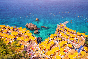 Aerial view of hidden narrow and cozy beach among cliffs and rocks with bright yellow umbrellas and...