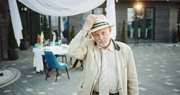 Mature man takes off hat greeting with light smile in cafe