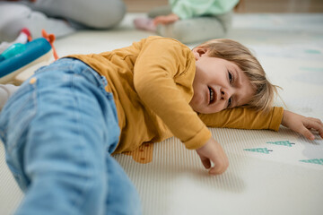 Sad little boy crying while lying down on floor at daycare.