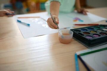 Close up of kid drawing with watercolor paints during art class at kindergarten.