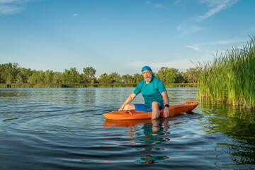 athletic, senior man is paddling a prone kayak on a lake in Colorado, this water sport combines aspects of kayaking and swimming