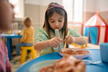 Little girl eats lunch at kindergarten.