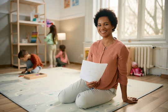 Happy Black Kindergarten Teacher Holding White Blank Paper And Looking At Camera.