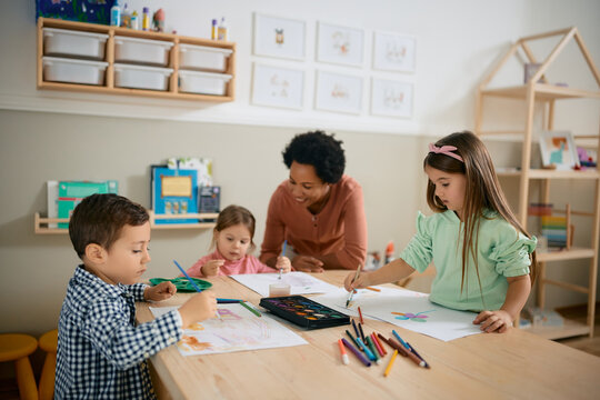Group of preschool kids and their teacher enjoy while coloring during art class.