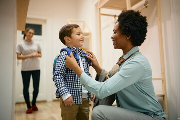 Happy African American mother adjusting son's backpack while leaving him at preschool for the first...