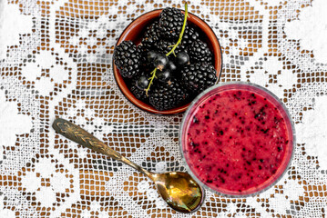 Blackberry smoothy in a glass and fresh blackberry in ceramic bowl.