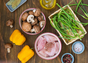 Prepared ingredients for cooking chicken stew with mushrooms, sweet peppers and garlic arrows on a wooden background. seasonal recipes.