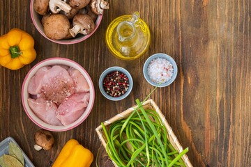 Prepared ingredients for cooking chicken stew with mushrooms, sweet peppers and garlic arrows on a wooden background. seasonal recipes.