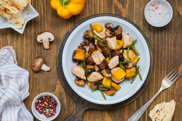 Chicken stew with mushrooms, sweet peppers and garlic arrows in a gray plate on a wooden background.