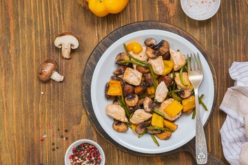 Chicken stew with mushrooms, sweet peppers and garlic arrows in a gray plate on a wooden background.