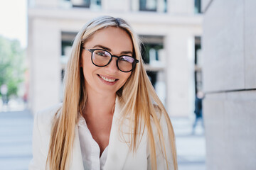 Portrait of cheerful young blonde Italian woman in glasses and white shirt outdoors, looking at camera with broad toothy smile. Happy swedish girl having break. Grateful employee loving her job.