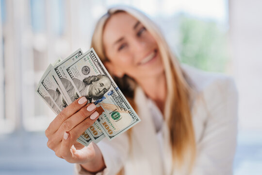 Dollar banknotes in hands of blurry cheerful beautiful blonde businesswoman offering money. Business salary and profit concept. Swedish female young woman holding money happy to get benefits.