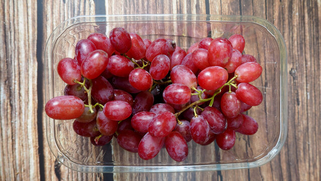 pink grapes in a plastic container stand on a brown wooden table.view from above. grona grapes