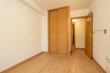 Empty room with built-in wardrobe with Venetian-style sliding oak wood doors and parquet floors of the same material