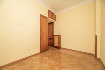 Empty bedroom with herringbone oak floor, light yellow painted walls and built in wardrobe with wooden door