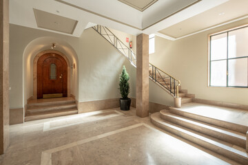 Stairs of a luxury house with marble stairs, tree in a pot and golden metal railing and a large window