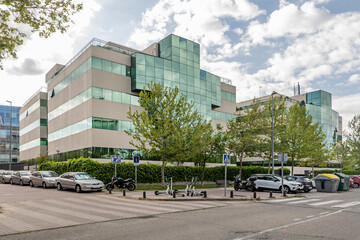 Facade of an office building with concrete and glass facades and gardens, a closed walkway and blue skies with some clouds