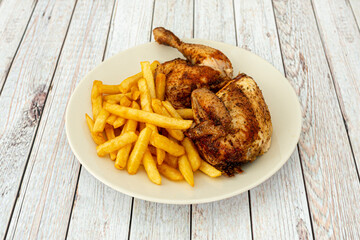 Half roasted chicken with french fries on a white plate and wooden table