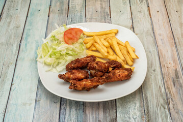 Menu plate fried chicken wings with salad and tomato and french fries served in a typical kebab restaurant