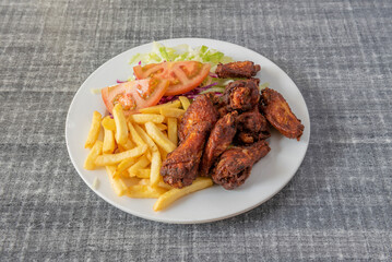 Fried chicken wings with salad and tomato and french fries served in typical kebab restaurant with white plate and gray table