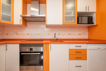 Kitchen with bright orange and white cabinets, drawers and ovens, orange stone countertop, gray...