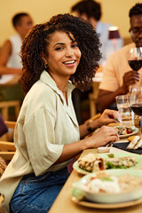 A multicultural young woman is sitting in a restaurant and having dinner.