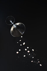 Martini style glass spilling over and pouring out a selection of drugs and or medication. Black background drug or medical concept with copy space