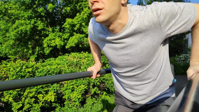 Young man trains on an outdoor sports field in city park. Guy does gymnastics on parallel bars. Biceps and triceps muscle training. Handsome bald man is doing push-ups. Healthy lifestyle