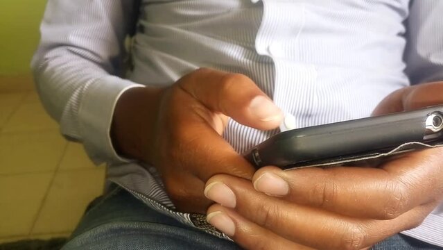 Close up of a young man busy working on his phone. He's wearing a striped official shirt. Business concept. Typing, texting, doing research. Copy space. At home. Using mobile phone footage.