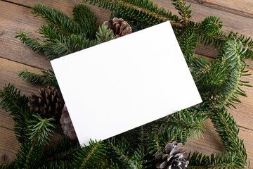 Christmas 7x5 card mockup template on natural fir twigs on wooden background. Design element for Christmas and New Year congratulation, rsvp, thank you, greeting or invitation card, sale