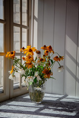 a fading bouquet of flowers in vase near window