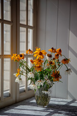 a fading bouquet of flowers in vase near window