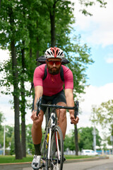 Fototapeta premium Strong Male cyclist in sportswear, glasses and protective helmet walking with his bike in the forest to take a break after riding. Sky blue and forest in the background.