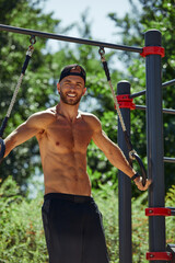 Obraz premium Young man exercising in an outdoor bodybuilding gym using gymnastic rings