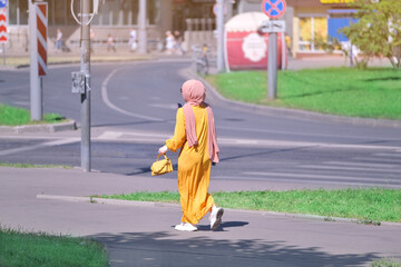 woman in a hijab, sneakers and a long yellow dress walks down the street in the city