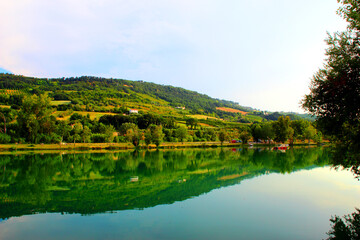 Park "I Due Laghi" in Piane di Moresco between the ridges of the typical serene and peaceful Marche hilly landscape with calm emerald waters of the lake, a tree silhouette and lush vegetation