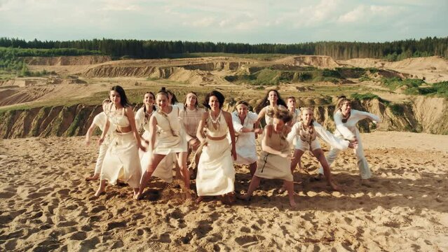 4k slow-mo group of women in white ethnic clothes dancing choreography on sand. Nature beautiful landscape. Blu sky and sunset light. Rural and boho style.